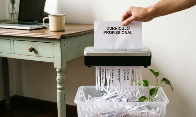 Um currículo sendo triturado sobre uma lixeira.